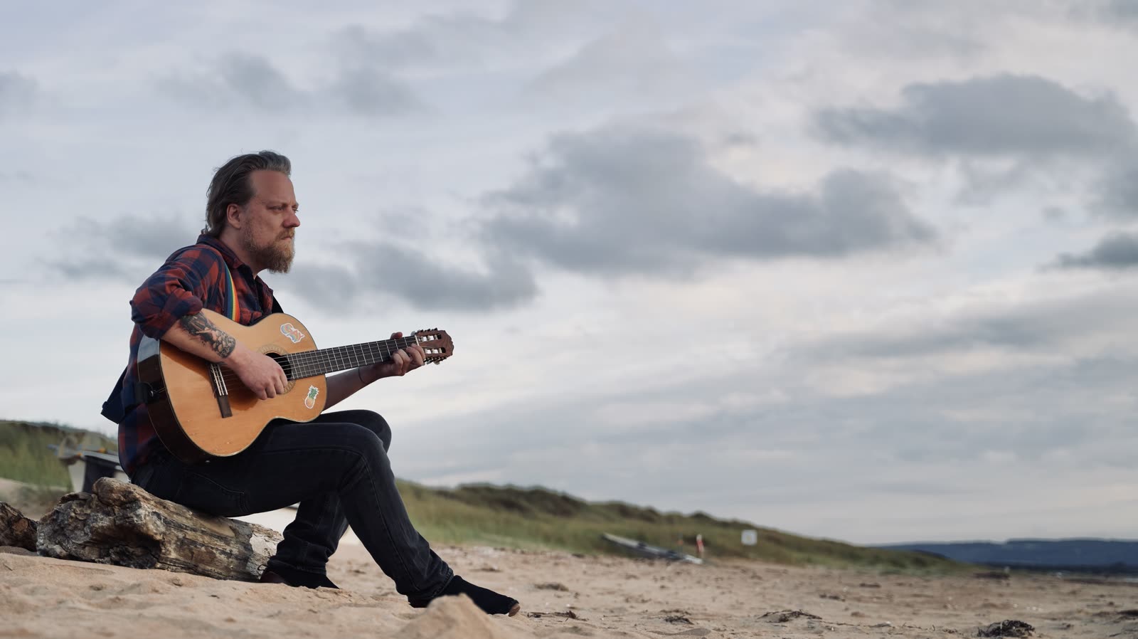David Guvå playing acoustic guitar on a beach